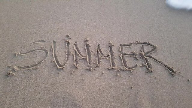 The word summer written on a sandy beach being washed away by ocean waves, summer is over