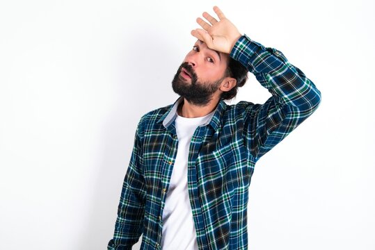 young bearded hispanic man wearing plaid shirt over white background wiping forehead with hand making phew gesture, expressing relief feels happy that he prevented huge disaster. It was close enough