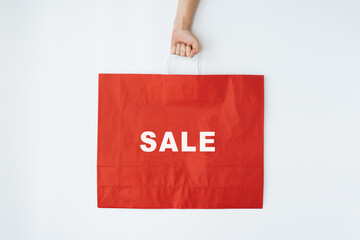 Fototapeta na wymiar Person's hand hold red craft shopping bag with sign SALE. Minimal Black Friday shopping, sale, promotion concept
