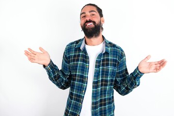 Fototapeta premium So what? Portrait of arrogant young bearded hispanic man wearing plaid shirt over white background shrugging hands sideways smiling gasping indifferent, telling something obvious.