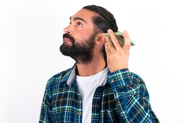 Smiling young bearded hispanic man wearing plaid shirt over white background listening a voice message from her smartphone. Communication and technology concept.