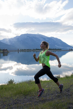 Young woman runs along edge of mtn lake, sunrise