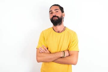 Self confident serious calm young bearded hispanic man wearing yellow T-shirt over white background...