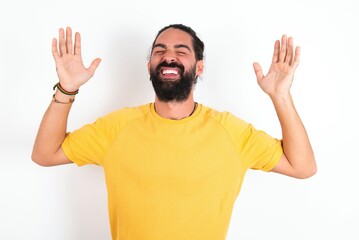 Fototapeta premium young bearded hispanic man wearing yellow T-shirt over white background goes crazy as head goes around feels stressed because of horrible situation