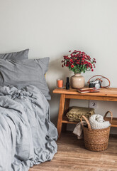 The interior of the bedroom - a bed with linen, a bouquet of red chrysanthemums on a wooden bench, a basket with plaid - a cozy homely atmosphere