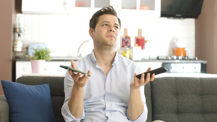 Overworked man with two smartphones in hand trying to keep up with unhappy online orders from...