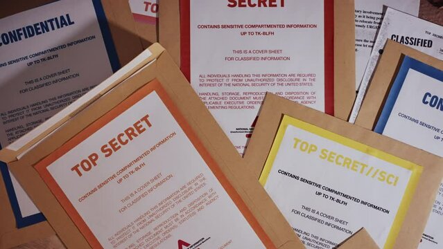 Top secret files in brown manila folders with warning cover sheets on desk. Different types of security clearance envelopes laid out on ground after police or agency raid. Evidence or leaked material