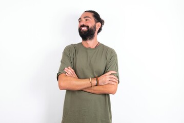 Fototapeta premium Dreamy rest relaxed young bearded hispanic man wearing green T-shirt over white background crossing arms, looks good copyspace