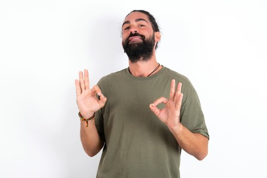 young bearded hispanic man wearing green T-shirt over white background showing both hands with fingers in OK sign. Approval or recommending concept