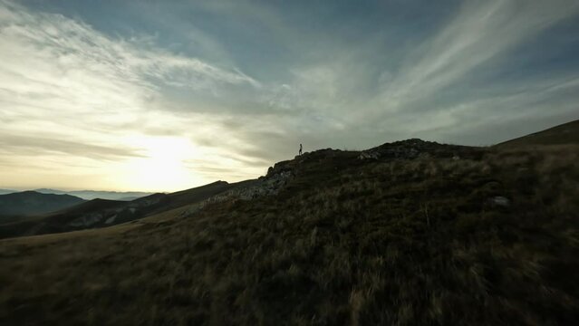 FPV drone flying past a cheerful female hiker enjoying the top of a mountain