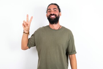 young bearded hispanic man wearing green t-shirt over white background showing and pointing up with fingers number two while smiling confident and happy.