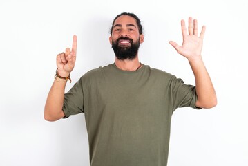 young bearded hispanic man wearing green t-shirt over white background showing and pointing up with fingers number six while smiling confident and happy.