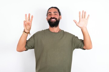 Fototapeta premium young bearded hispanic man wearing green t-shirt over white background showing and pointing up with fingers number eight while smiling confident and happy.