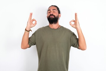 Fototapeta premium young bearded hispanic man wearing green t-shirt over white background relax and smiling with eyes closed doing meditation gesture with fingers. Yoga concept.