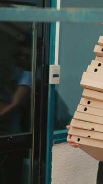 Vertical video: Fastfood meal courier dropping pizza boxes pile outside building, clumsy takeaway worker stumbling and running scared. Bad delivery service, pizzeria employee with falling packages