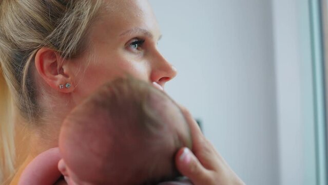 Beautiful indoor portrait of young Caucasian blonde woman lightly touching the head of her infant son. Bond between mother and child. High quality 4k footage