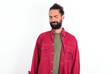 Dismal gloomy rejected Caucasian man with beard wearing red shirt over white background has problems and difficulties, curves lower lip and closes eyes in despair, being in depression