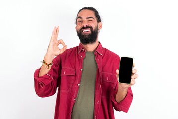 Caucasian man with beard wearing red shirt over white background holding in hands cell showing...