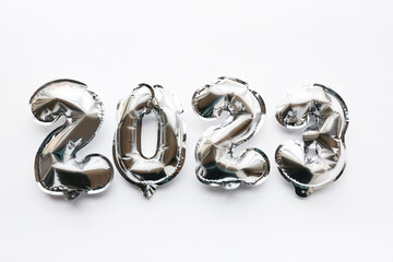 Obraz na płótnie Canvas Balloons made of silver foil in the form of numbers 2023 on a white background. Celebrating Christmas, New Year and festive concept. Flat lay, top view.
