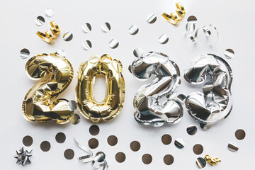 Silver and gold foil balloons in the form of numbers 2023 on a white background with festive confetti. Celebrating Christmas, New Year and holiday concept. Flat lay, top view.