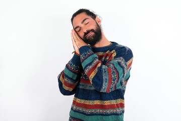 Caucasian man with beard wearing sweater over white background leans on pressed palms closes eyes and has pleasant smile dreams about something