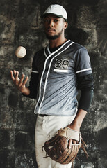 Baseball, sports and uniform with a man athlete on a dark background wearing a mitt while holding a ball. Portrait, sport and confident with a male baseball player standing against a dugout wall © Allistair/peopleimages.com