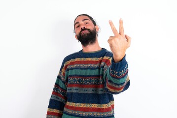 Naklejka premium Caucasian man with beard wearing sweater over white background smiling and looking friendly, showing number two or second with hand forward, counting down