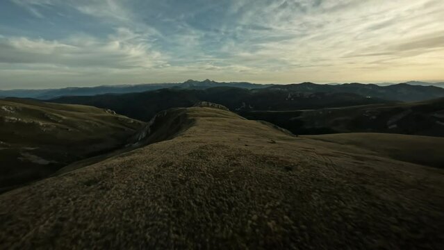 FPV drone flying past a cheerful female hiker enjoying the top of a mountain