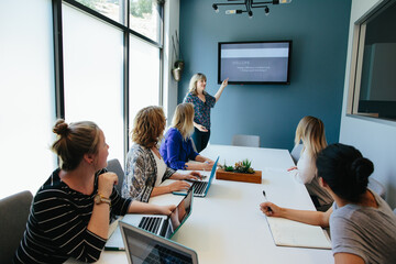Women sitting at a conference table look and listen to woman standing