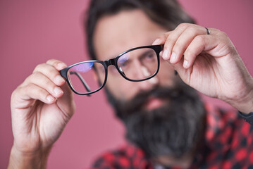Checking his glasses, shortsighted bearded man examining his spectacles, blurred person behind the glasses - 541013232