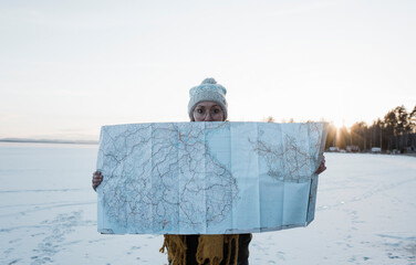 woman holding up a large map whilst standing on a frozen lake