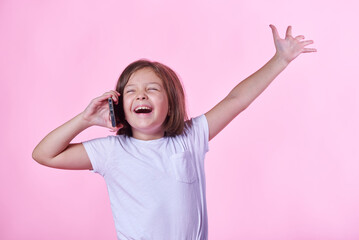 Excited little girl getting great, winning news over her phone; pink studio background