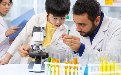 male teacher sitting at classroom desk with male student using microscope while learning science experiment