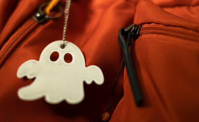 Key chain reflector in ghost pattern form on orange backpack, security sign to protect pedestrian...