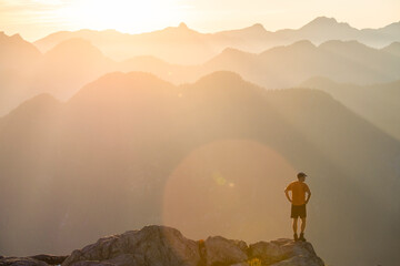 Trail runner standing on edge of a mountain cliff at sunset.
