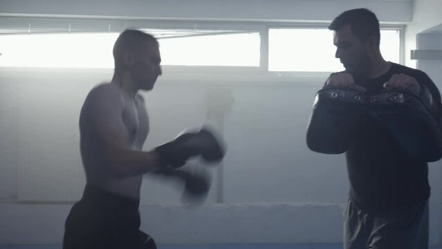Kickboxing coach training fighter, teaching attack punches and defense technique handheld medium shot. Fighting instructor and kickboxer practicing, exercising in sport club