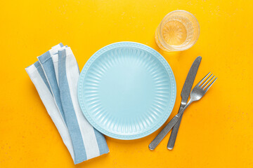 Empty blue plate, table textile and cutlery on yellow background. Table setting with copy space for...