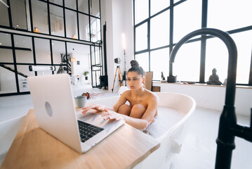 Young woman working on laptop while taking a bathtub