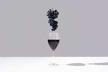 Copa de vino tinto y racimo de uvas negras sobre fondo gris	