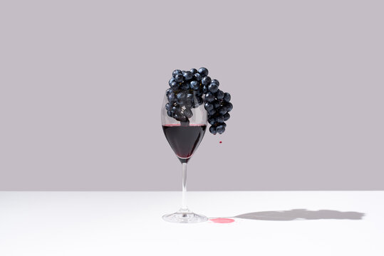 Copa de vino tinto y racimo de uvas negras sobre fondo gris	