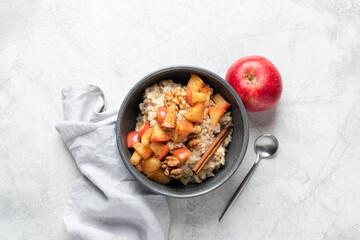 Breakfast oatmeal with apple cinnamon and walnuts in bowl on grey concrete table background, top view. Seasonal autumn comfort food