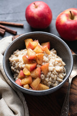 Caramelized apple cinnamon oatmeal porridge bowl on wooden serving board, closeup view, healthy breakfast food