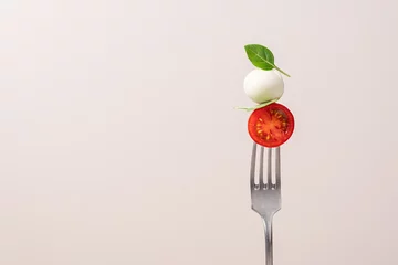 Fotobehang Fork with tomato, mozzarella cheese and basil. Caprese salad on fork close up view. Italian food concept © Anna Puzatykh