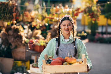 Farmer woman holds a wooden box with pumpkins in hands