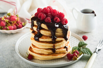 American pancakes. Stack pancakes with fresh raspberry with chocolate glaze or toppings in white bowl on light gray table background. Homemade classic american pancakes. Magazine concept. Top view.