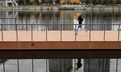 Morning running workout on the bridge near the river. A young man in warm sportswear runs in the city. The concept of a healthy lifestyle, fitness, sport.