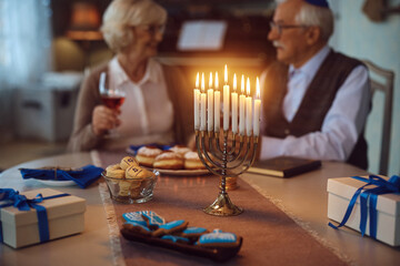Traditional Hanukkah menorah candles with senior couple in background.