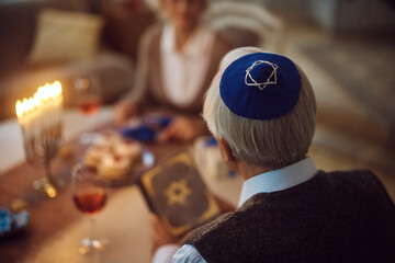 Close up of senior Jewish man reading Tanakh while celebrating Hanukkah with his wife at home.