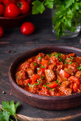 Chashushuli, thick beef stew in tomato sauce with sweet pepper, onion and spices in a clay bowl on a dark wooden background. Beef recipes.