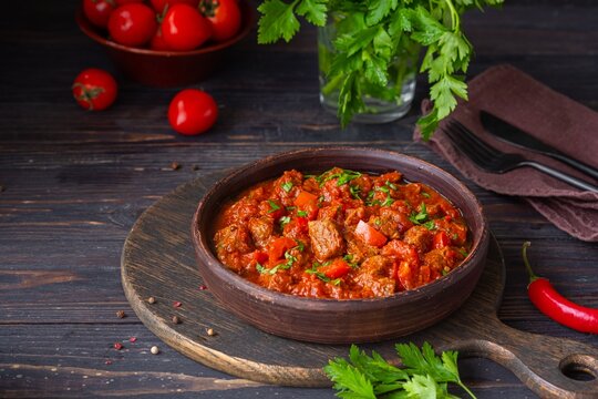 Chashushuli, thick beef stew in tomato sauce with sweet pepper, onion and spices in a clay bowl on a dark wooden background. Beef recipes.